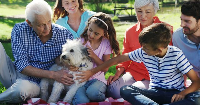 A multigenerational family, including grandparents, parents, and children, are sitting on a picnic blanket in a park with their pet dog. They are enjoying their time together, smiling, and petting the dog, which adds a happy atmosphere to the scene. This can be used for promoting family values, outdoor activities, pet-friendly places, summer leisure activities, and bonding moments.