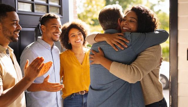 Daughter hugging father while family applauding at home during sunny reunion