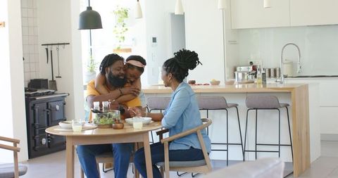 African family sharing warm breakfast hug around dining table in modern minimalist kitchen