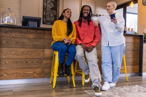Diverse friends laughing and chatting at cozy coffee counter on yellow stools, casual