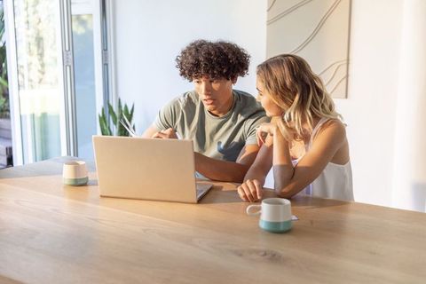 Young couple collaborating on laptop at sunlit modern dining table for remote work and planning