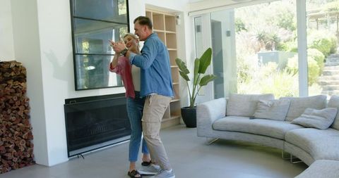 Mature couple dancing in sunlit contemporary living room near fireplace