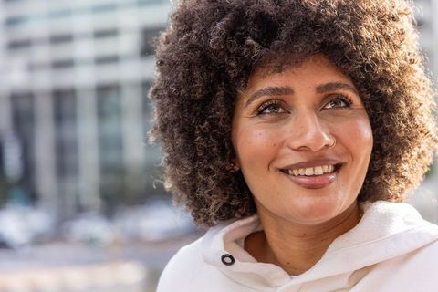 Smiling woman looking upward on city street wearing white hoodie and hoop nose ring