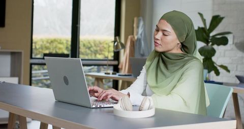 Indian professional woman in green hijab working on laptop in modern coworking space