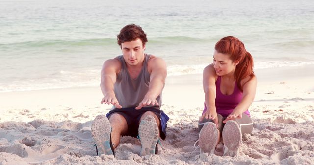 Couple stretching on a sandy beach during sunrise. Ideal for promoting fitness, healthy lifestyles, morning workout routines, well-being and outdoor recreational activities.