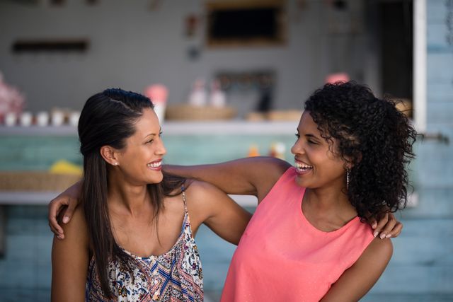 Two women smiling and interacting outdoors, showcasing joy and friendship. Ideal for use in lifestyle blogs, social media posts, advertisements promoting friendship and togetherness, and content related to leisure and casual gatherings.
