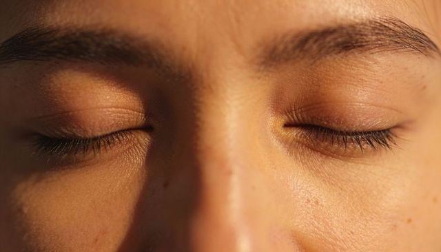 Woman resting with closed eyes in warm golden light, highlighting eyelashes, freckles and pores