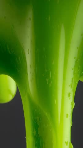 Flowing slow-motion green viscous liquid ribbon with glossy droplets in vertical video