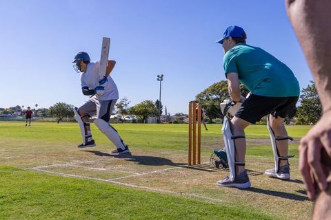 Amateur cricketer batting on sunny community field with wicket-keeper positioned