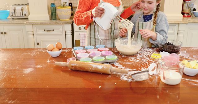 Happy mother and daughter bonding while baking cupcakes in cozy kitchen. Ideal for themes involving family activities, baking, home cooking, and parent-child relationships. Can be used for cooking blogs, family-oriented advertisements, or educational materials on cooking with kids.