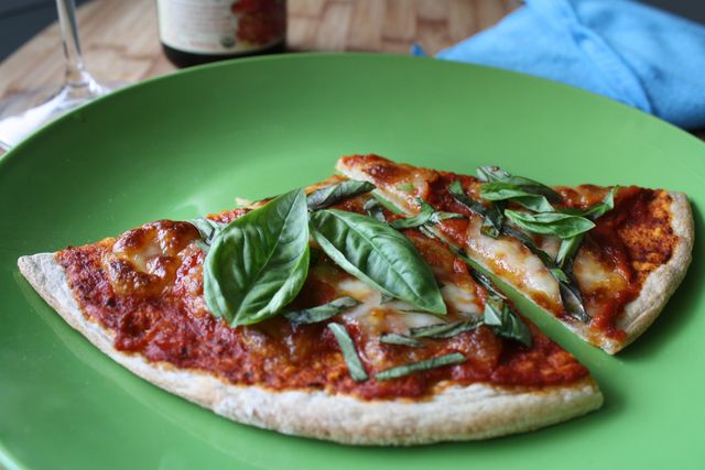 Slices of Margherita pizza topped with fresh basil are served on a vibrant green plate. Ideal for use in food blogs, cooking websites, recipe tutorials, Italian cuisine promotions, or restaurant menus. Perfect for emphasizing fresh ingredients and mouth-watering presentation.