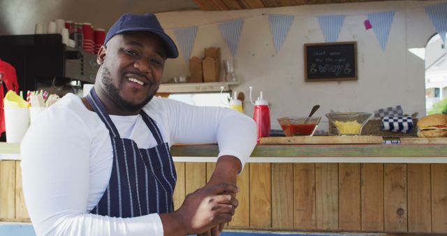 Portrait of african american man wearing apron smiling while standing near the food truck. food truck and street food concept