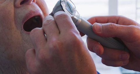 Doctor examining senior patient with otoscope during pandemic
