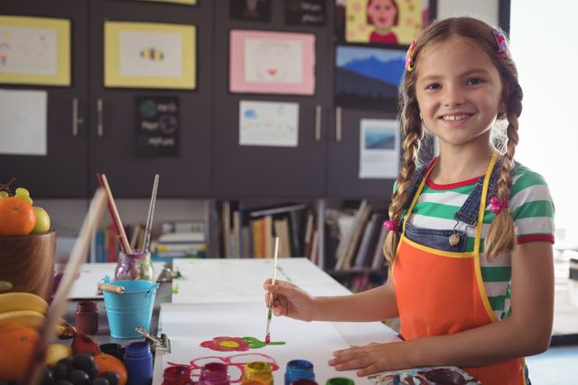 Portrait of smiling girl painting at desk in classroom