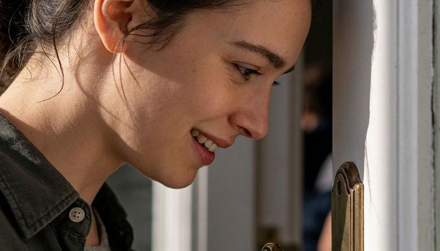 Young woman inspecting brass door lock closeup profile curious smile warm natural light