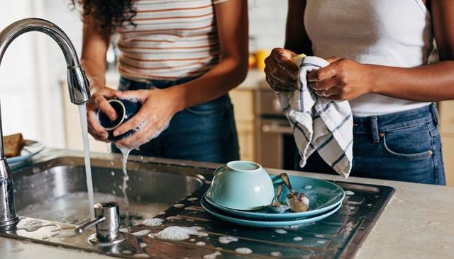 Two women washing dishes together at kitchen sink with chrome faucet and turquoise plates