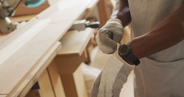 Mid section of african american male carpenter wearing safety gloves in a carpentry shop. carpentry, craftsmanship and handwork concept