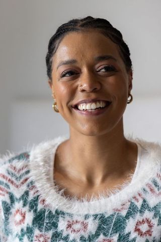 Smiling african american woman wearing fluffy patterned sweater, braided hair and gold hoop earrings