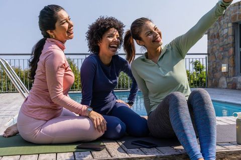 Diverse women taking selfie after poolside yoga session, laughing and bonding outdoors