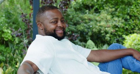 African man reclining on garden bench smiling in white shirt and blue jeans