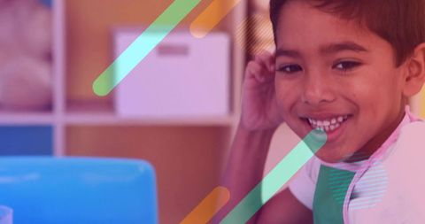 Smiling boy wearing green apron sitting at table learning in classroom with graphic overlays