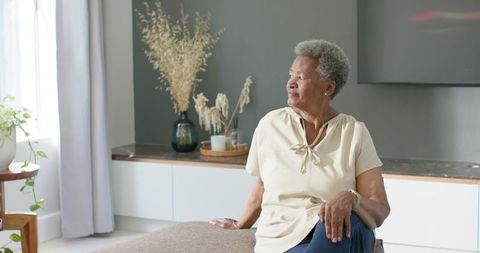 Senior african american woman sitting peacefully, gazing at sunlit window in minimalist interior