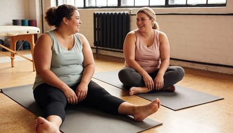 Plus-size women chatting and relaxing on yoga mats in sunlit wellness studio