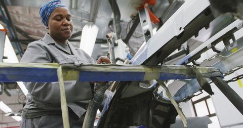 Female technician inspecting automotive panel on assembly line in industrial workshop