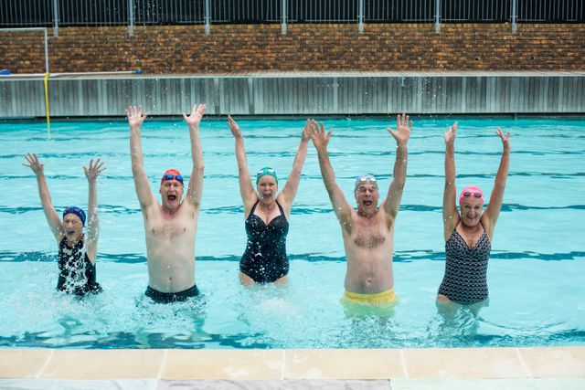 Group of senior swimmers having fun in a swimming pool, raising arms and splashing water. Perfect for promoting active lifestyles, senior fitness programs, health and wellness campaigns, and leisure activities for the elderly.
