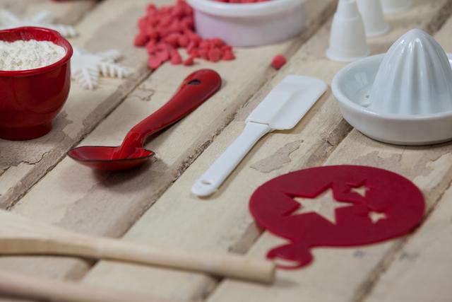 This image showcases a close-up view of various baking tools and ingredients arranged on a wooden board. It includes a red spoon, a white spatula, a bowl of flour, and other baking accessories. Ideal for use in culinary blogs, holiday baking articles, kitchen tool advertisements, or festive recipe books.