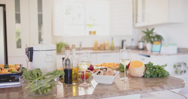 Modern kitchen counter filled with healthy cooking ingredients. Fresh vegetables, herbs, and olive oil are elegantly arranged alongside wine glasses. Ideal for use in food blogs, healthy lifestyle promotions, and culinary magazines to illustrate nutritious meal preparation.