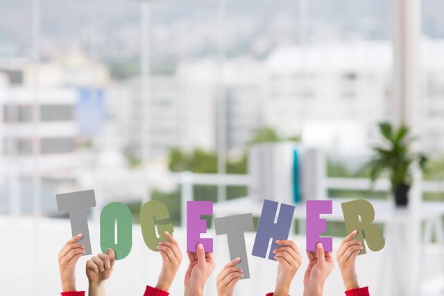 Hands of multiple individuals holding colorful letters spelling 'TOGETHER' against a blurred urban background. Ideal for concepts of teamwork, unity, collaboration, and community support. Useful for promotional materials, social campaigns, and educational content emphasizing the importance of working together.