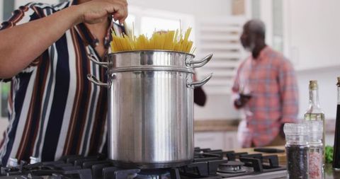 Woman stirring spaghetti in stainless steel stockpot on gas stove, homestyle pasta cooking