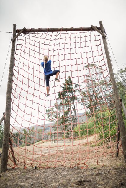 Woman climbing a net during obstacle course in boot camp