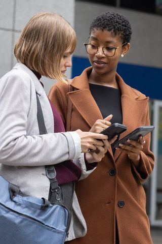 Two colleagues checking smartphones and comparing notes outside modern office building