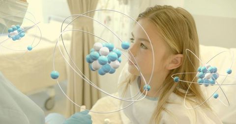 Gown-clad child observing virtual atomic models during pediatric checkup promoting STEM curiosity