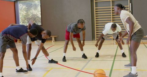Basketball players stretching hamstrings during indoor team warm-up and conditioning