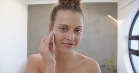 Woman practicing skincare with cotton pad in minimalistic room