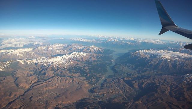 Aerial panorama of snow-capped mountains, winding river and airplane winglet