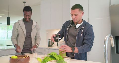 Diverse friends preparing green smoothie in modern kitchen showcasing healthy lifestyle