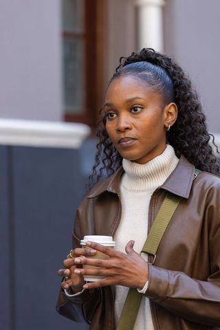 African american woman standing on urban sidewalk holding coffee cup wearing leather jacket