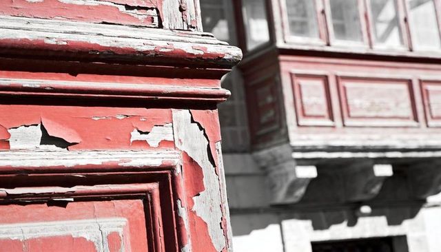 Peeling red wooden molding on historic facade revealing weathered timber texture, ornamental detail