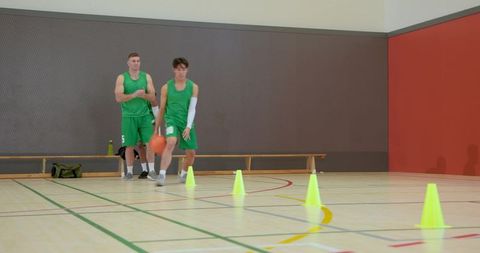 Male basketball players dribbling through cones in gym practicing agility and teamwork