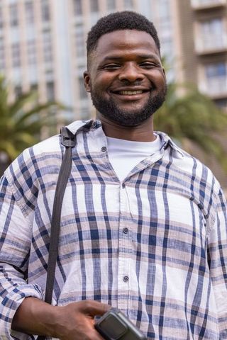 African american man smiling with smartwatch and backpack in urban plaza lifestyle portrait