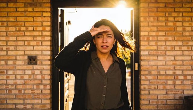 Woman shielding eyes from sunlight in brick doorway during golden hour