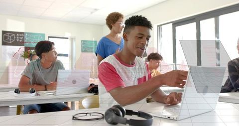 High school teens collaborating on laptops in bright classroom with teacher guidance