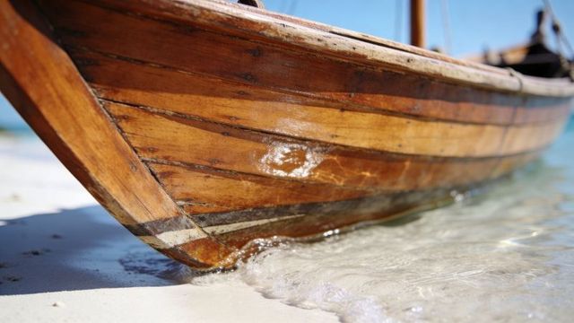 Glinting varnished wooden boat hull resting on clear shallow water and white sand