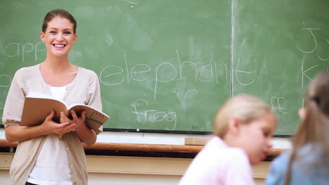 Smiling Teacher Reading Open Book in Classroom