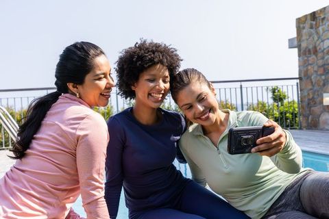 Three women taking selfie poolside in activewear, smiling and enjoying sunny friendship