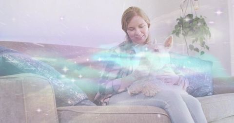 Young woman cuddling small white dog on sofa with dreamy aurora overlay